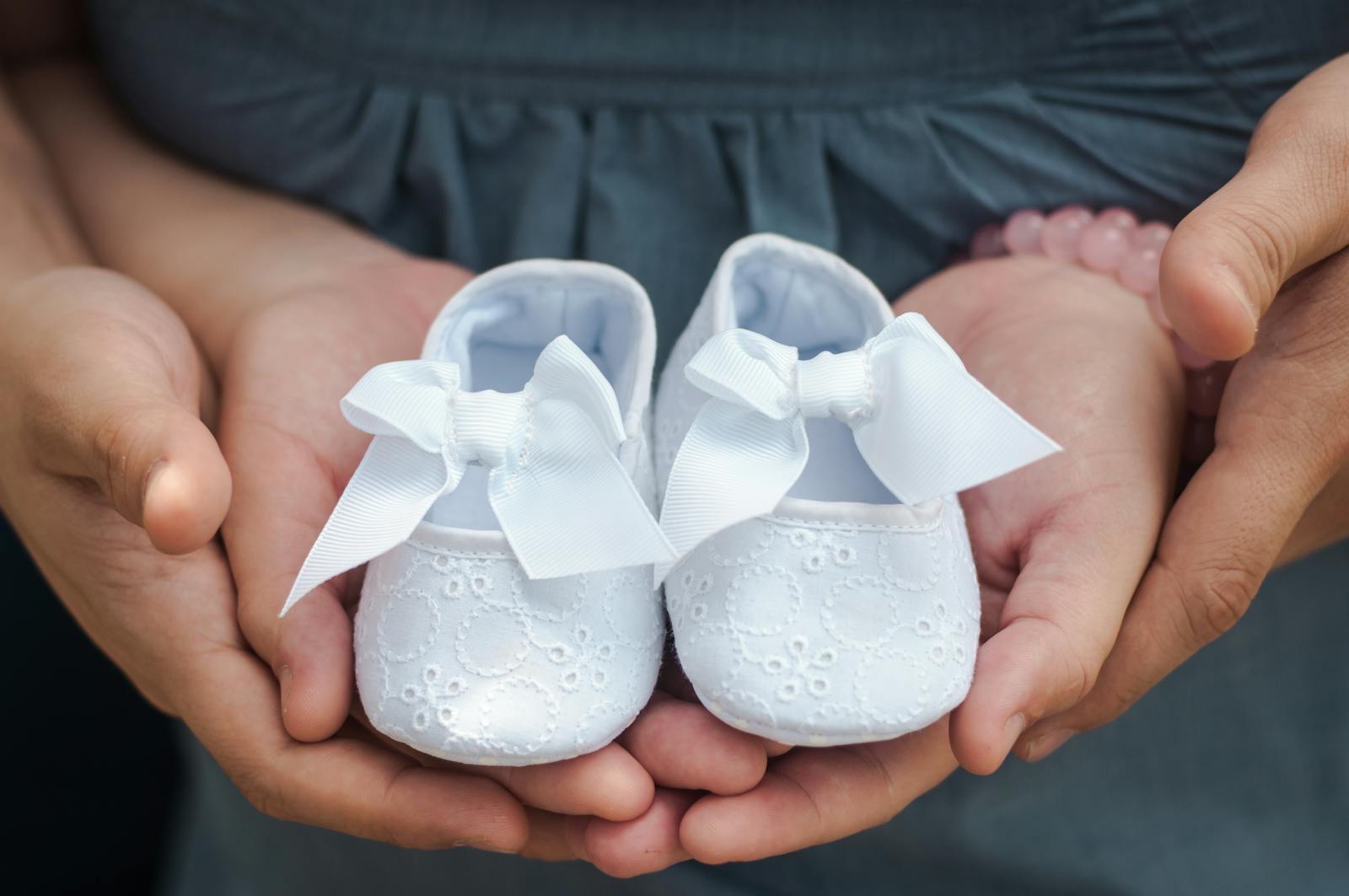 Close-up photo of hands holding white baby shoes with delicate bows, showcasing love and anticipation.